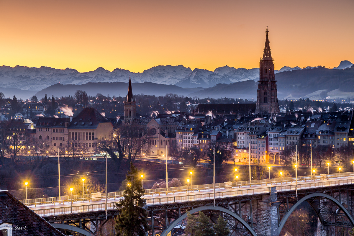 Stadtpanorama Bern mit Münster und beleuchteter Aarebrücke bei Dämmerung, Alpen im Hintergrund, Winter in der Schweiz – Jan Geerk Fotograf Basel