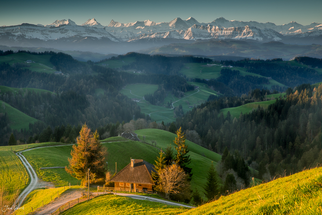 Alpenhof in der Lüderenalp mit Blick auf die schneebedeckten Berner Alpen im Frühling, grüne Wiesen und Wälder im Emmental, Schweiz – Jan Geerk Fotograf Basel