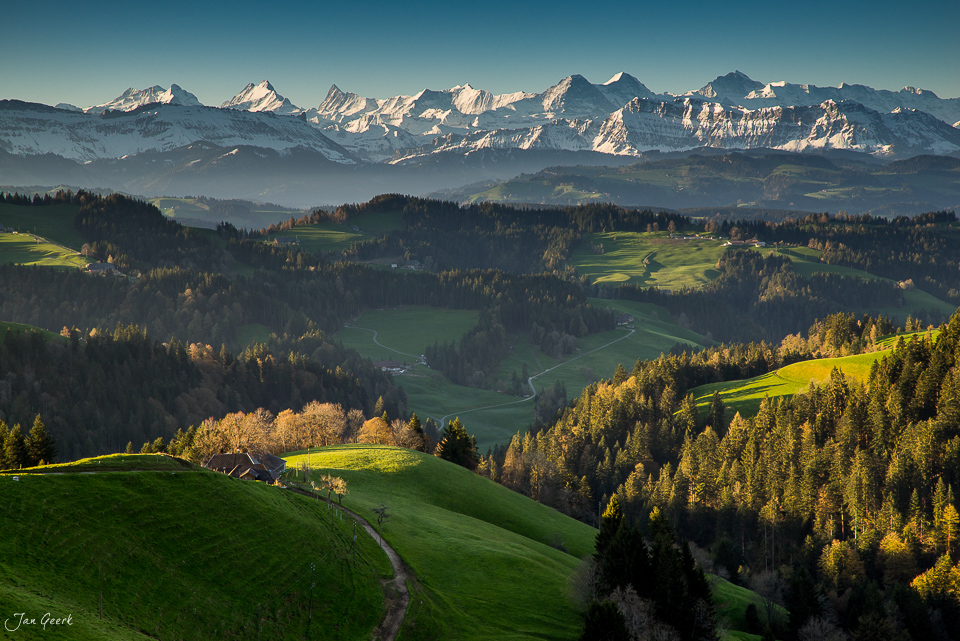 Alpweiden und Wälder im Emmental mit Blick auf schneebedeckte Berneralpen, Frühjahr, Berner Oberland Schweiz – Jan Geerk Fotograf Basel