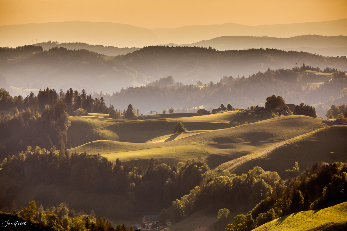 Hügelige Landschaft im Emmental mit golden beleuchteten Feldern, Wäldern und Bergketten in Sommerlicht – Schweiz, Jan Geerk Fotograf Basel