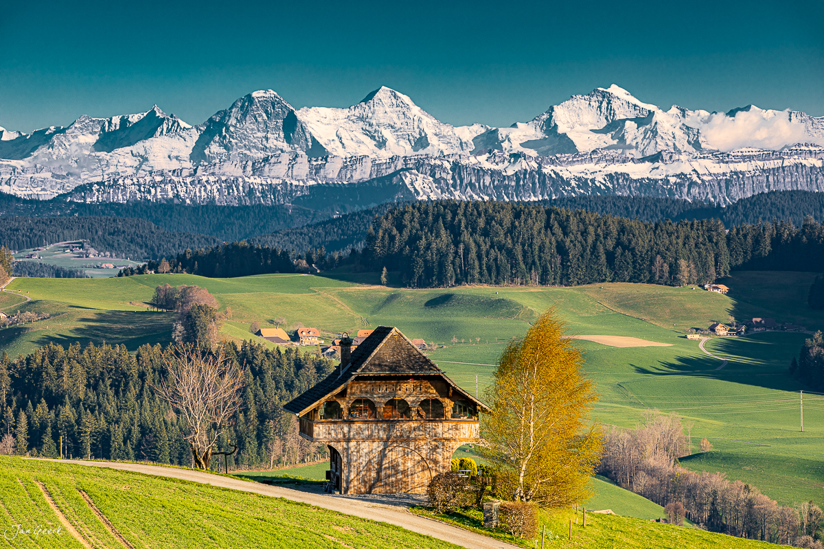 Historisches Emmentalhaus mit Eiger, Jungfrau und Mönch im Hintergrund, Frühlingslicht, Berner Oberland Schweiz – Jan Geerk Fotograf Basel