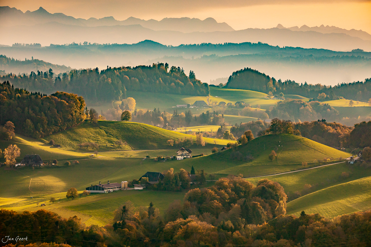 Herbstliche Hügellandschaft im Emmental mit golden beleuchteten Wiesen, Bauernhöfen und Alpenblick, Schweiz – Jan Geerk Fotograf Basel