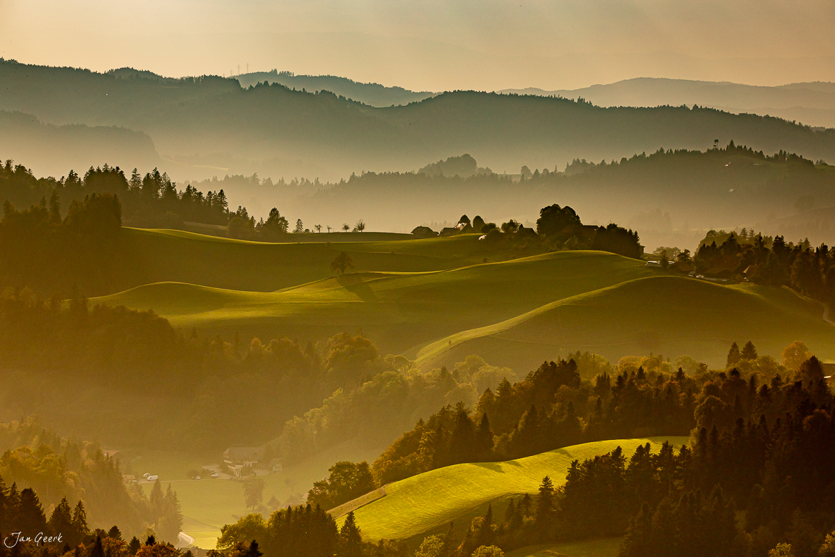 Hügelige Emmental Landschaft bei Kantlicht mit nebligen Bergen dahinter Schweiz Jan Geerk Fotograf Basel