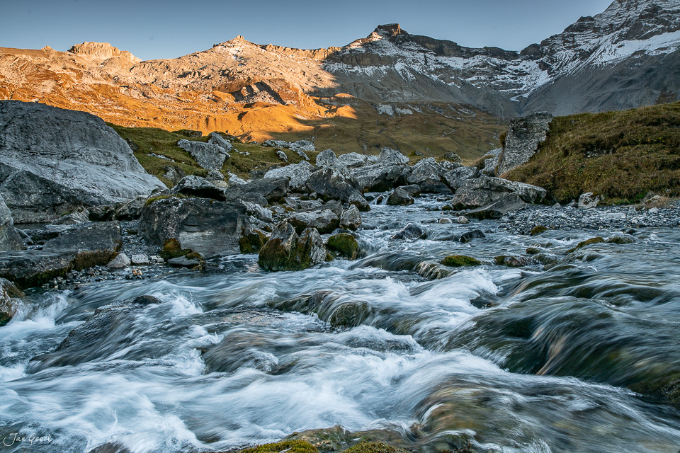 Engstligenalp Bergbach mit Felsen im Herbstlicht, schneebedeckte Berge im Hintergrund, Berner Oberland Schweiz – Jan Geerk Fotograf Basel