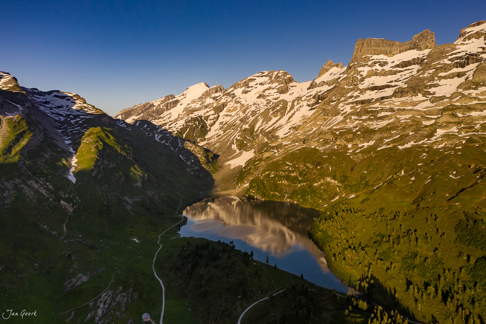 Luftaufnahme des Engstlensees mit schneebedeckten Bergen und grünen Alpweiden im Sommer, Berner Oberland Schweiz – Jan Geerk Fotograf Basel