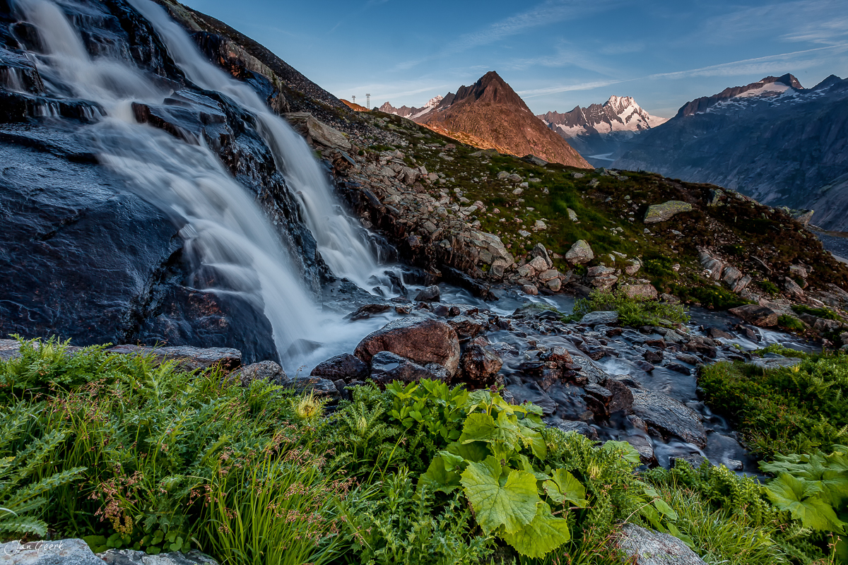 Wasserfall und Bergbach am Grimselpass mit schneebedeckten Alpengipfeln im Hintergrund, Berner Oberland Schweiz – Jan Geerk Fotograf Basel