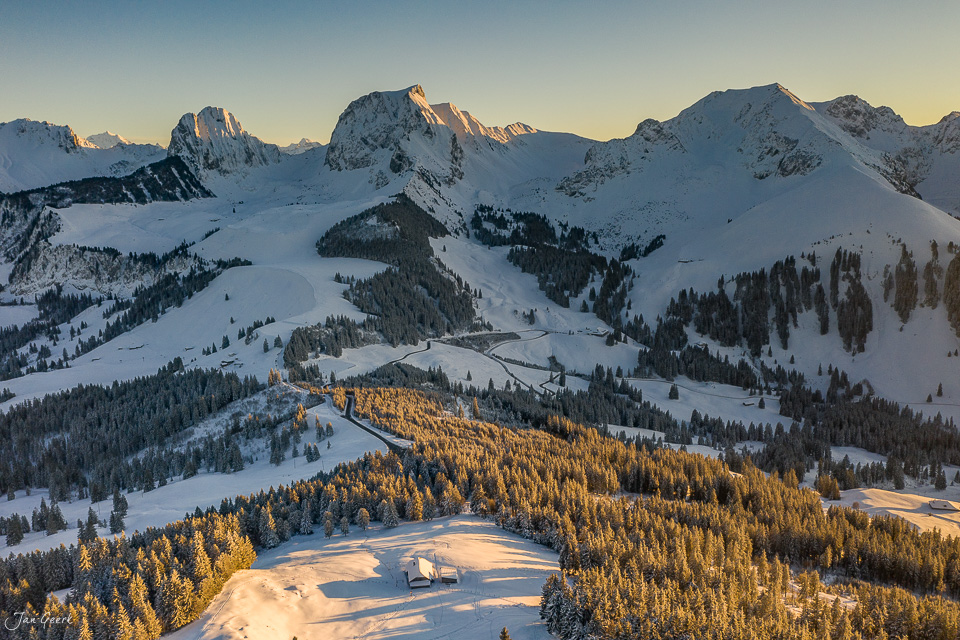 Winterliche Luftaufnahme des Gurnigel mit verschneiten Bergen, Lärchenwald in Kantlicht und Oberland-Panorama Schweiz – Jan Geerk Fotograf Basel