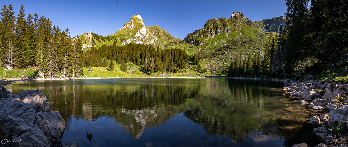 Alpensee mit Spiegelung von Berggipfeln und Nadelwald im Sommer, Gantrischseeli Berner Oberland Schweiz – Jan Geerk Fotograf Basel
