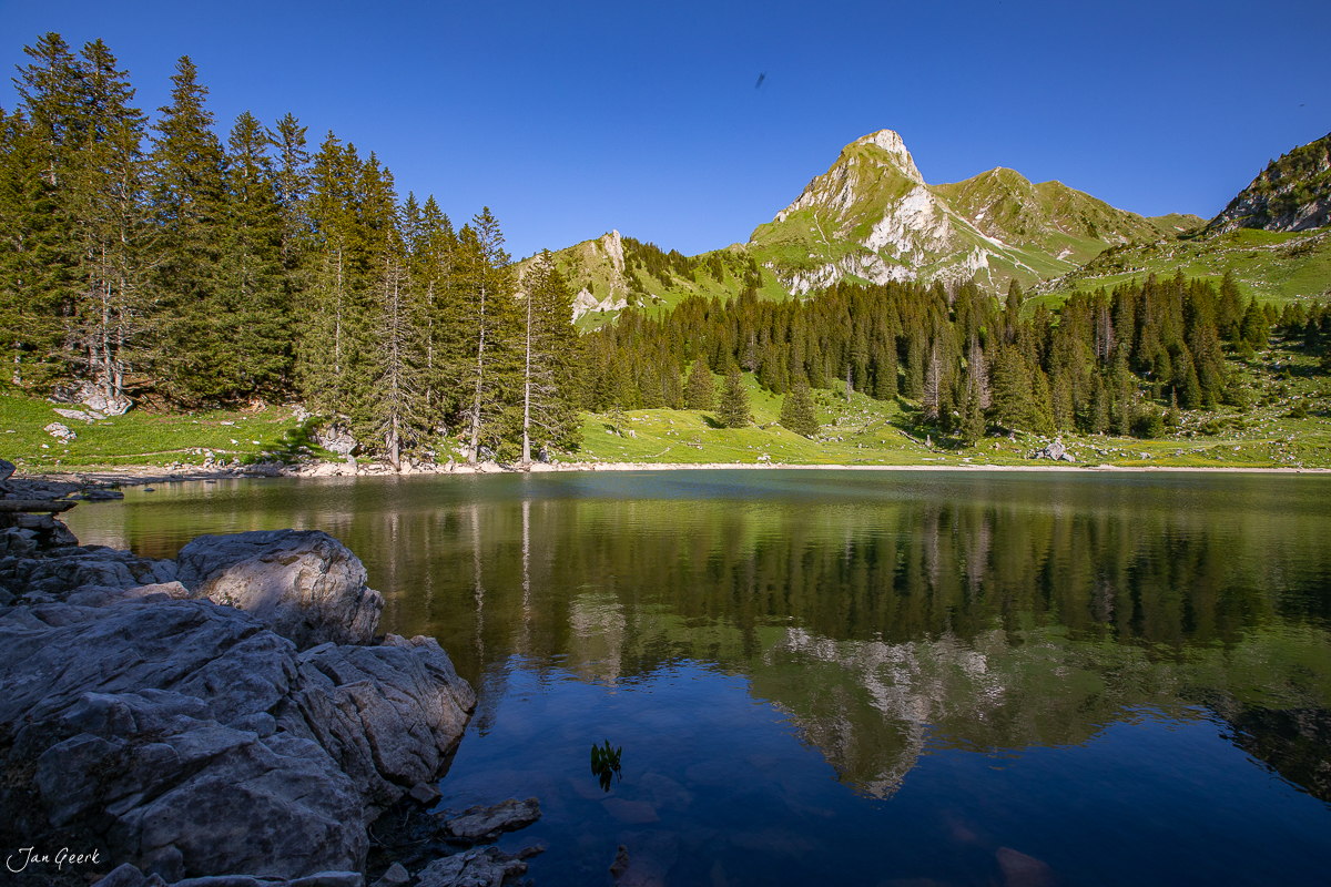 Gurnigel See mit Spiegelbild der Berge, grüne Lärchenwälder und Kalkfelsen im Berner Oberland Sommer Schweiz – Jan Geerk Fotograf Basel