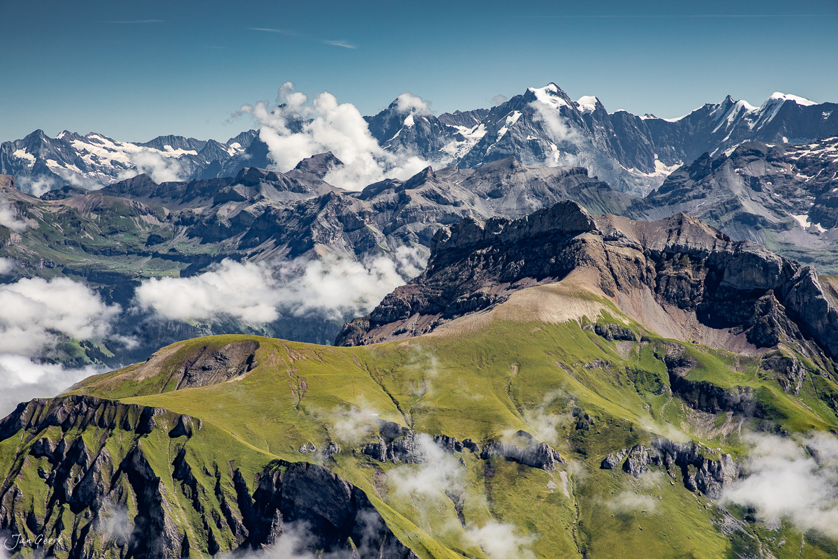 Luftaufnahme der Alpen im Berner Oberland mit grünen Alpweiden, schneebedeckten Gipfeln und Wolken im Sommer, Schweiz – Jan Geerk Fotograf Basel