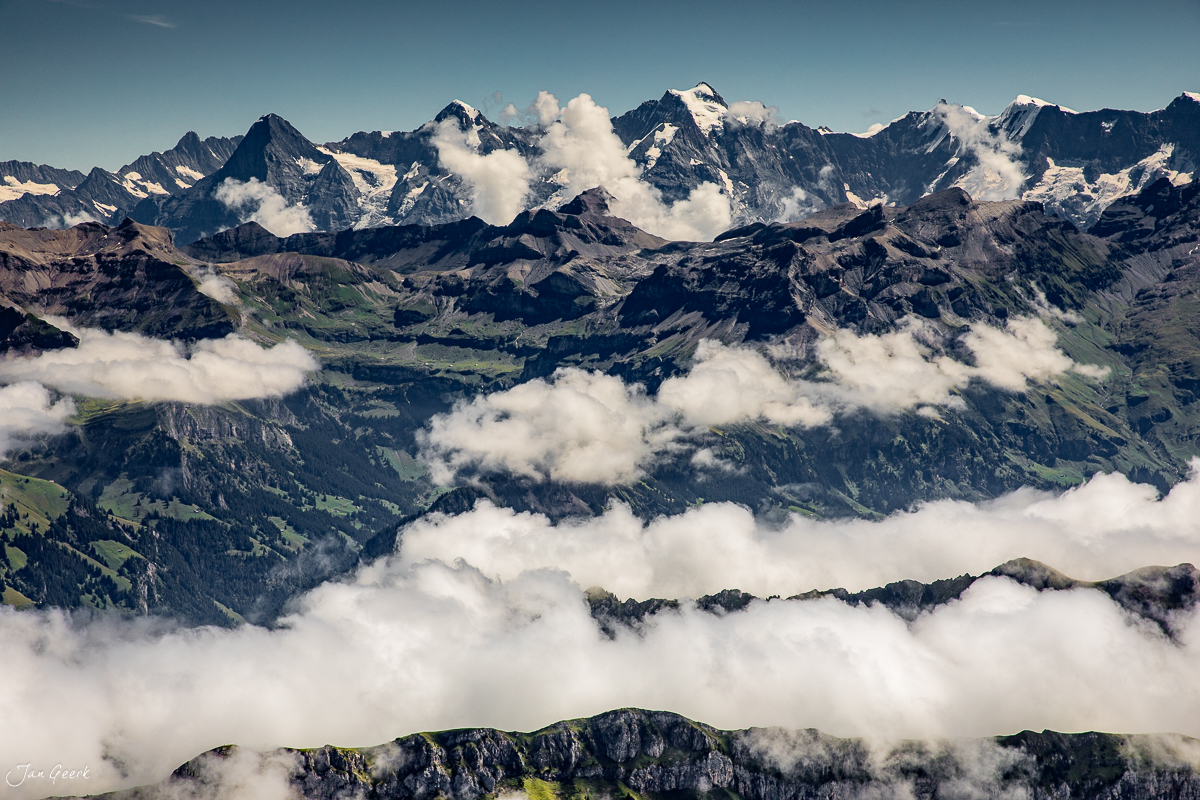 Luftaufnahme Berner Oberland mit schneebedeckten Alpen, grünen Alpweiden und Wolkendecke im Sommer, Schweiz – Jan Geerk Fotograf Basel