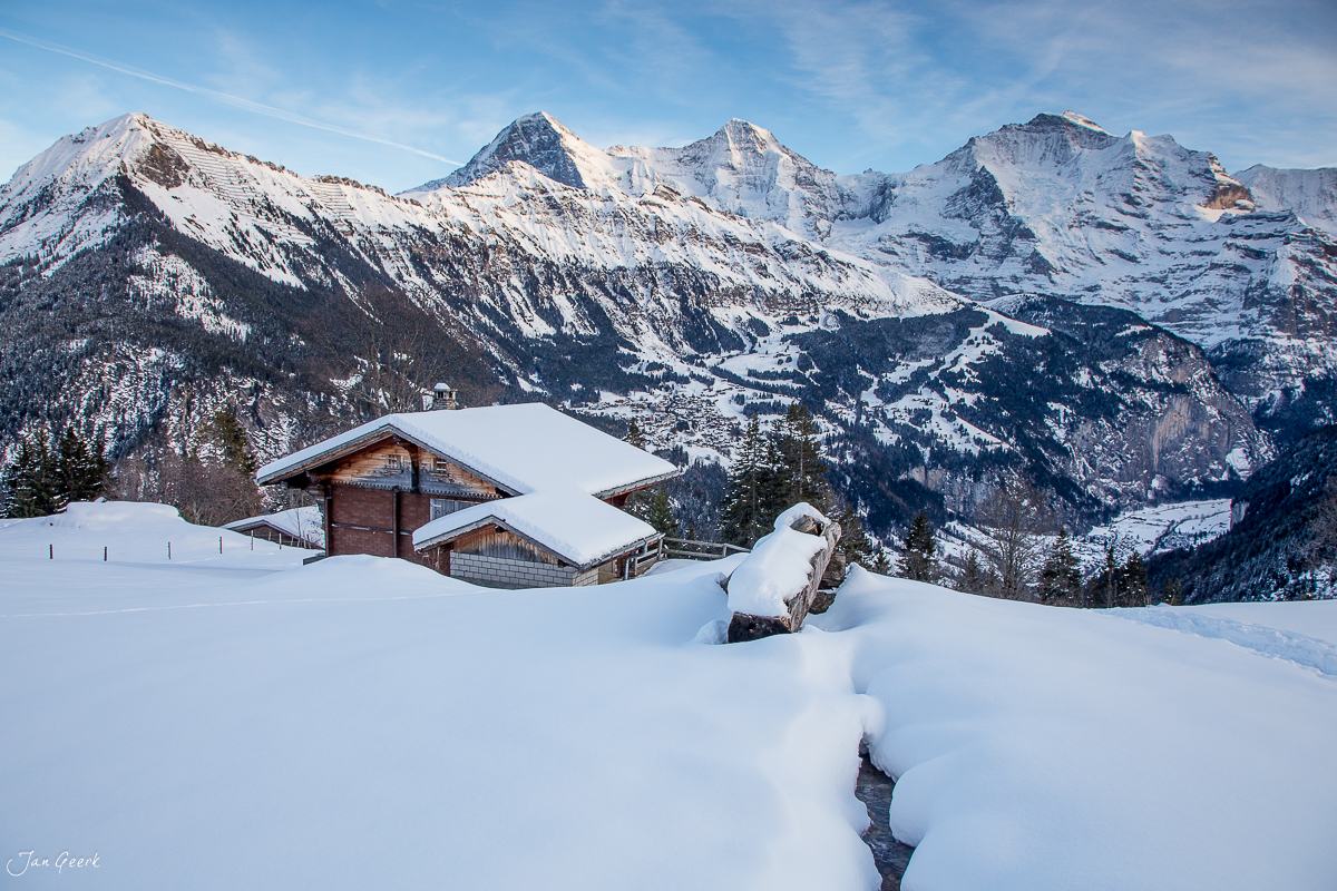 Verschneite Alphütte im Oberland mit schneebedeckten Bergspitzen im Hintergrund, Winterlandschaft Schweiz – Jan Geerk Fotograf Basel