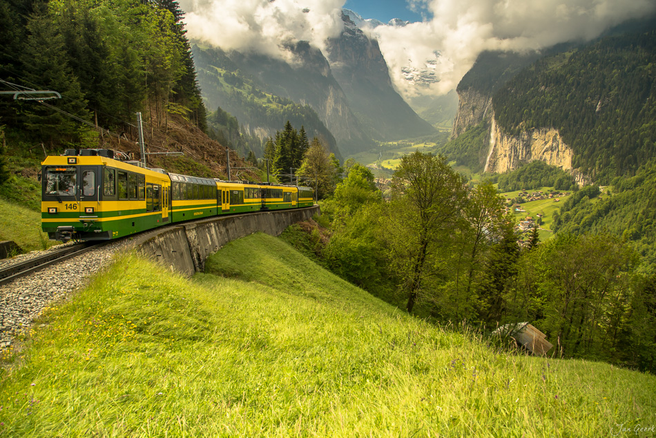 Gelber Zahnradbahn-Zug fährt durch grünes Tal mit steilen Bergen im Frühling in Lauterbrunnen, Schweiz – Jan Geerk Fotograf Basel