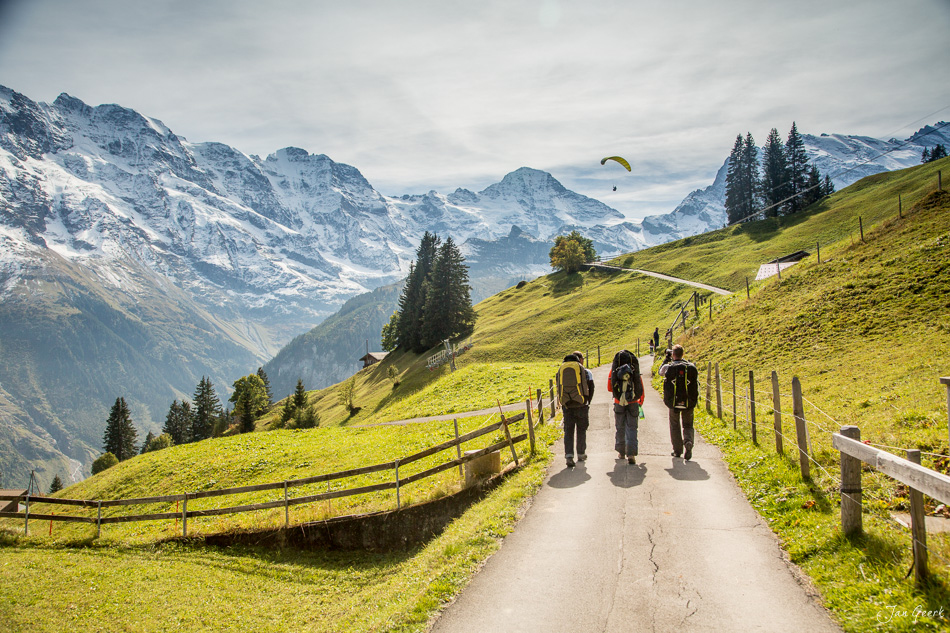 Wanderer auf Bergweg in Lauterbrunnen mit schneebedeckten Alpen, grüne Wiesen, Gleitschirm, Sommer, Berner Oberland Schweiz – Jan Geerk Fotograf Basel