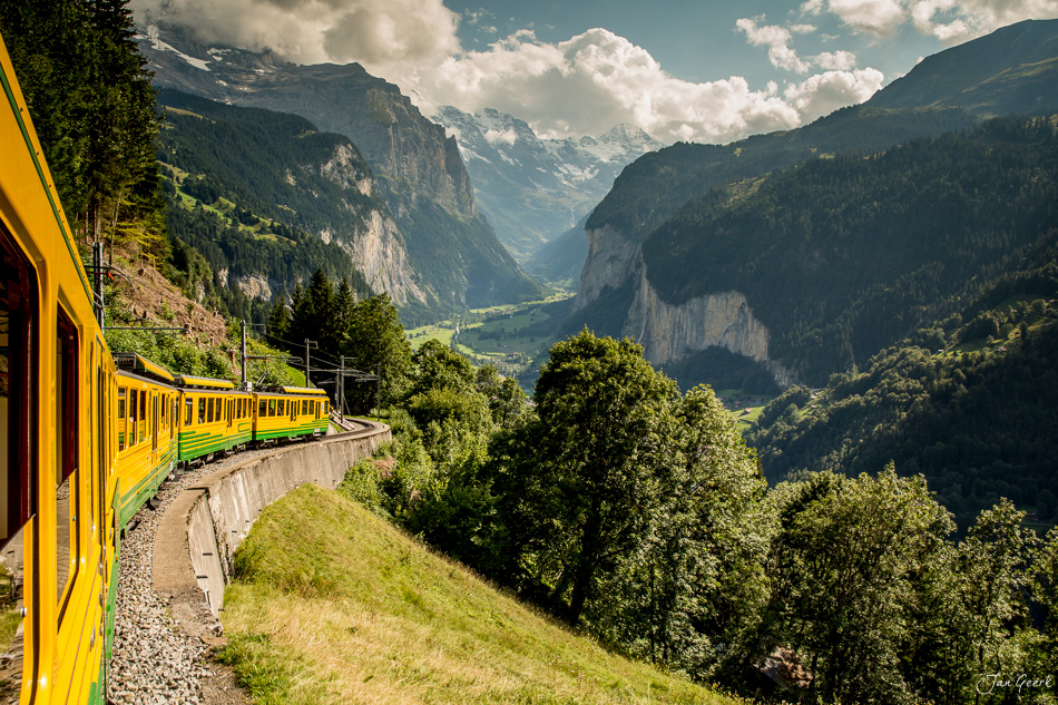 Gelber Zug fährt durch Lauterbrunnen Tal mit dramatischen Felswänden und Alpenlandschaft unter blauem Himmel Schweiz Jan Geerk Fotograf Basel