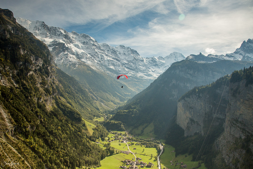 Gleitschirmflieger über dem Lauterbrunnen Tal mit schneebedeckten Alpen, grünen Wiesen und Bergdörfern, Sommer in der Schweiz – Jan Geerk Fotograf Basel