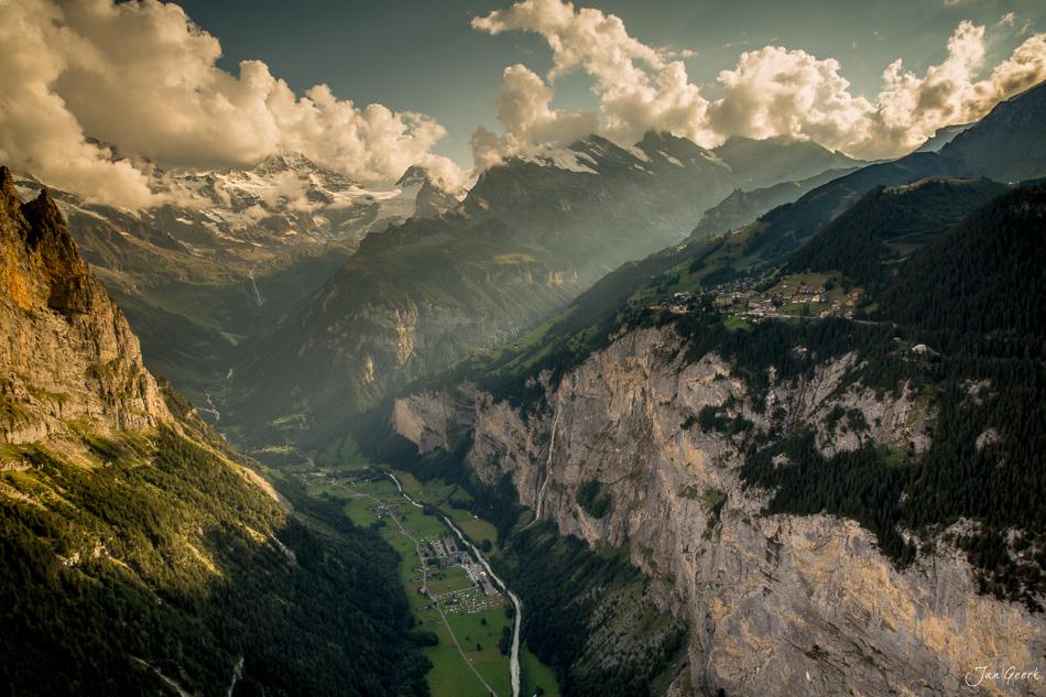 Luftaufnahme des Lauterbrunnentals mit steilen Felswänden, grünen Wiesen und schneebedeckten Alpengipfeln unter dramatischem Sommerhimmel – Berner Oberland Schweiz, Jan Geerk Fotograf Basel
