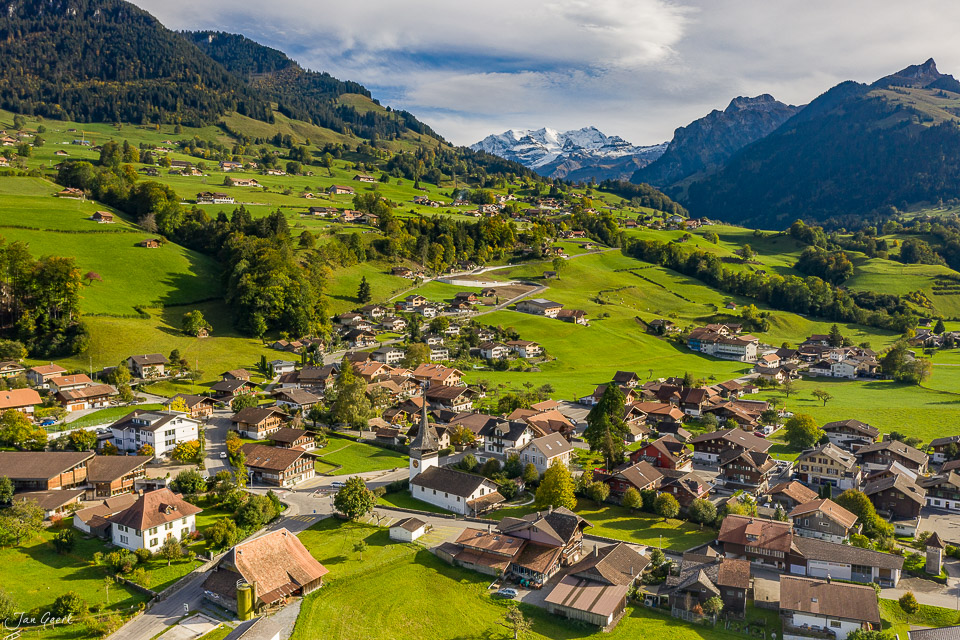 Luftaufnahme des Dorfes Reichenbach im Kandertal mit grünen Wiesen, Berghängen und schneebedeckten Alpengipfeln im Hintergrund – Berner Oberland Schweiz – Jan Geerk Fotograf Basel