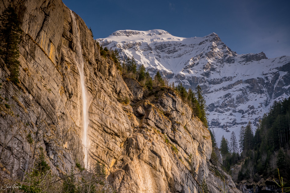 Wasserfall an Felswand mit verschneitem Eiger im Hintergrund, Berner Oberland Winter Schweiz – Jan Geerk Fotograf Basel