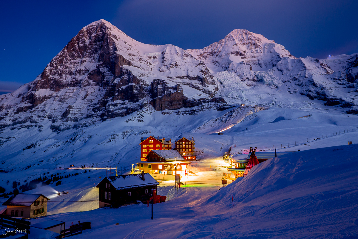 Beleuchtete Alphütten bei Scheidegg mit schneebedecktem Eiger im Hintergrund, winterliche Alpennacht in der Schweiz – Jan Geerk Fotograf Basel