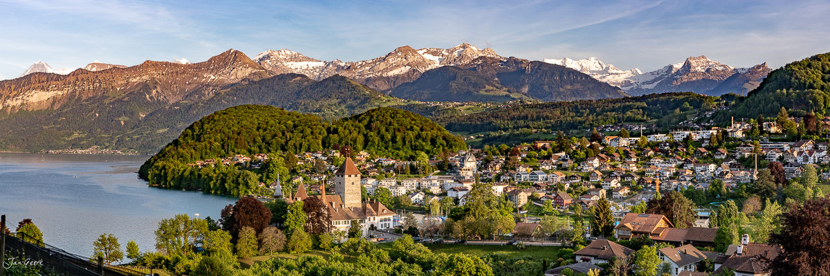 Luftaufnahme Schloss Spiez am Thunersee mit Rebbergen, Alpenpanorama im Hintergrund, goldenes Kantlicht, Frühling, Berner Oberland, Schweiz – Jan Geerk Fotograf Basel