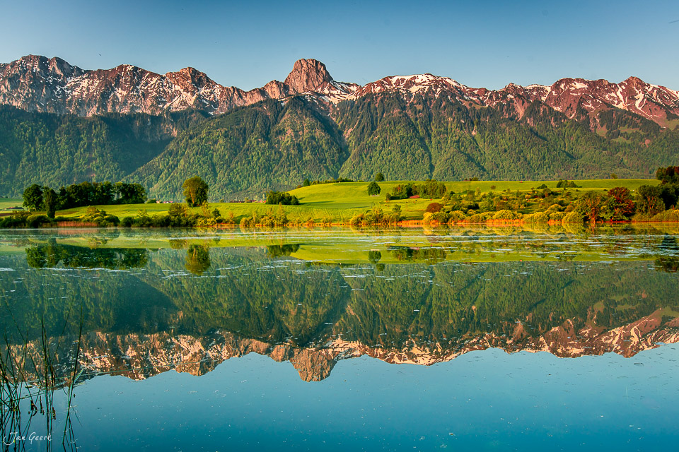 Spiegelung des Stockhorn in ruhigem Wasser beim Übeschisee, grüne Alpweiden und Bergwald im Sonnenlicht, Berner Oberland Schweiz – Jan Geerk Fotograf Basel
