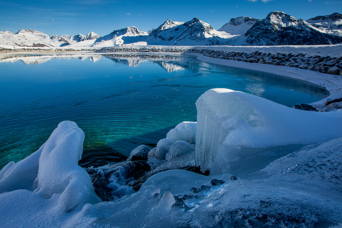 Gefrorener See mit Eiskristallen und schneebedeckte Berge im Hintergrund, Arosa, Graubünden, Winterstimmung Schweiz – Jan Geerk Fotograf Basel