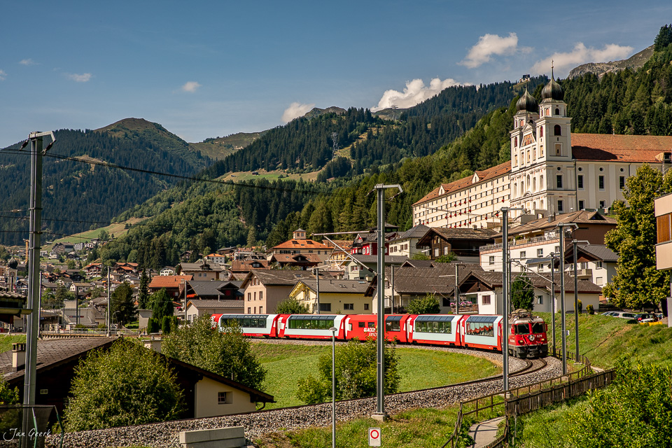 Roter Zug vor Kloster Disentis mit Alpenbergen im Sommer, Graubünden Schweiz – Jan Geerk Fotograf Basel