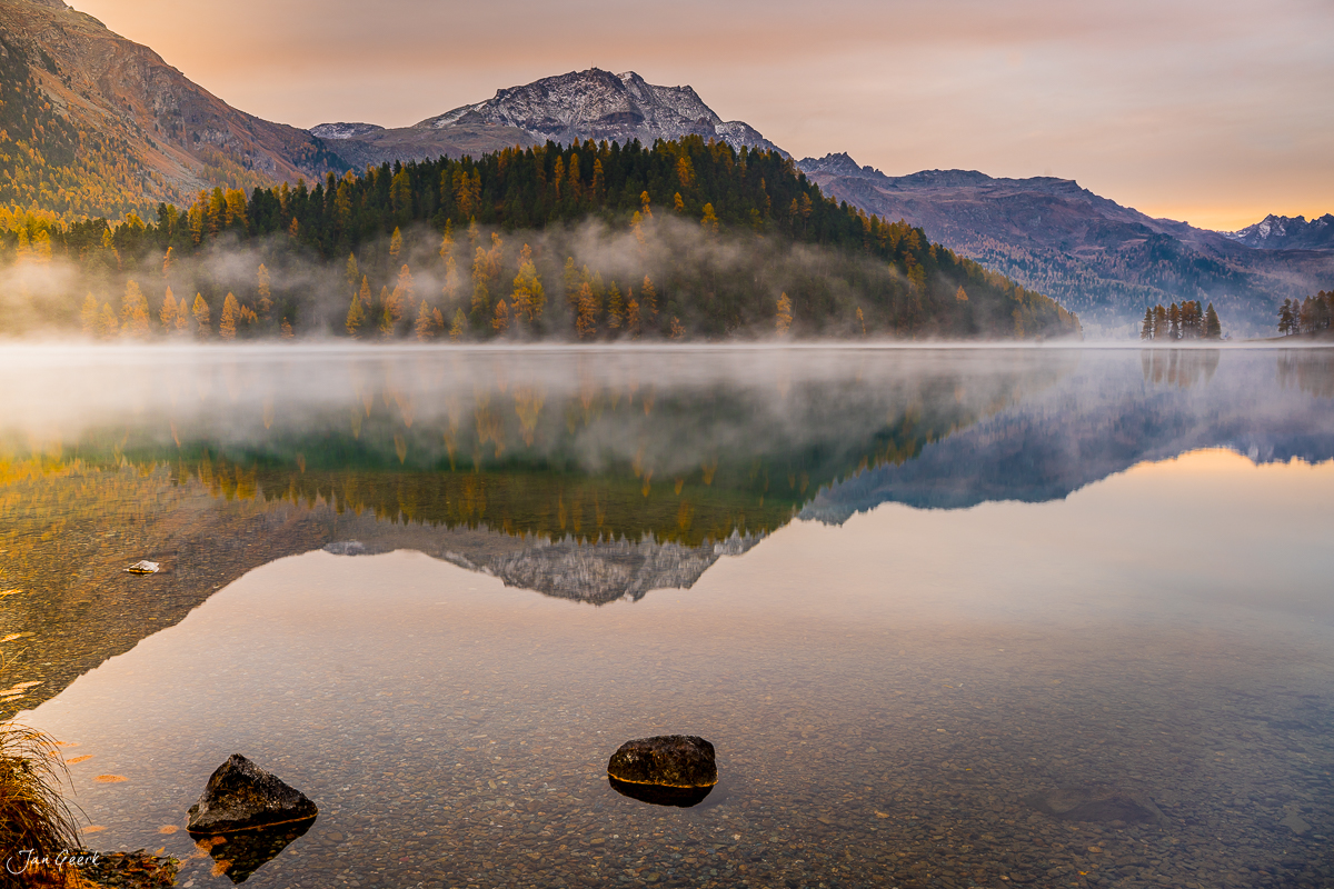 Spiegelglatter See mit Herbstlärchen und schneebedeckten Bergen im Engadin, goldene Morgenstimmung, Graubünden Schweiz – Jan Geerk Fotograf Basel