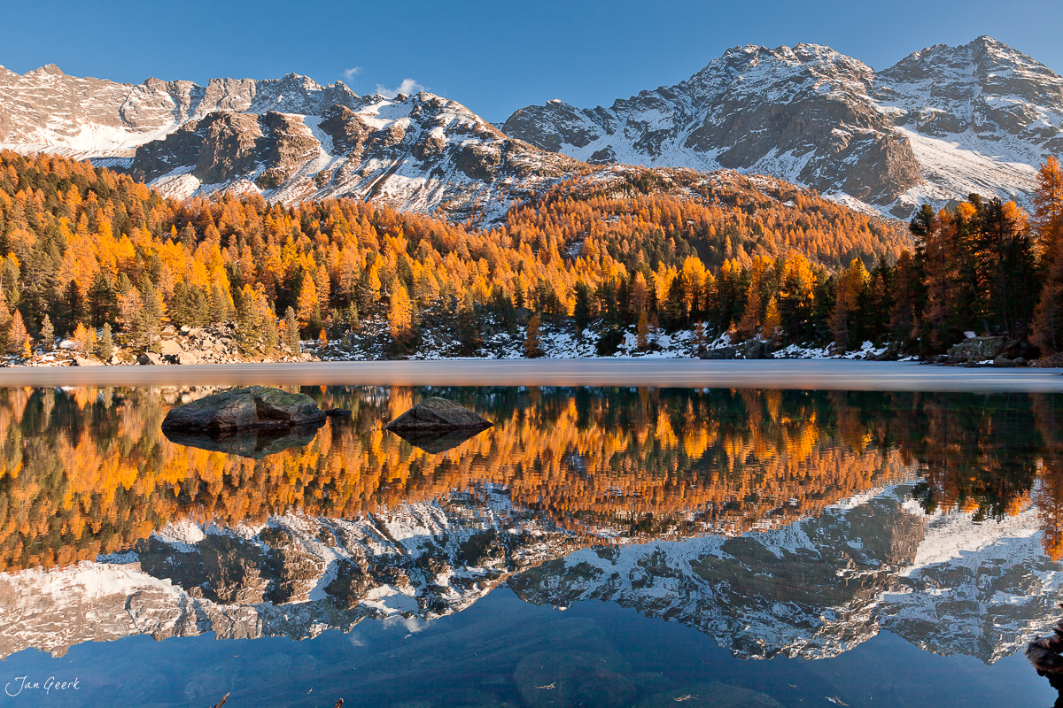 Herbstliche Lärchenwälder spiegeln sich in alpinem Bergsee Engadin Graubünden Schweiz Jan Geerk Fotograf Basel