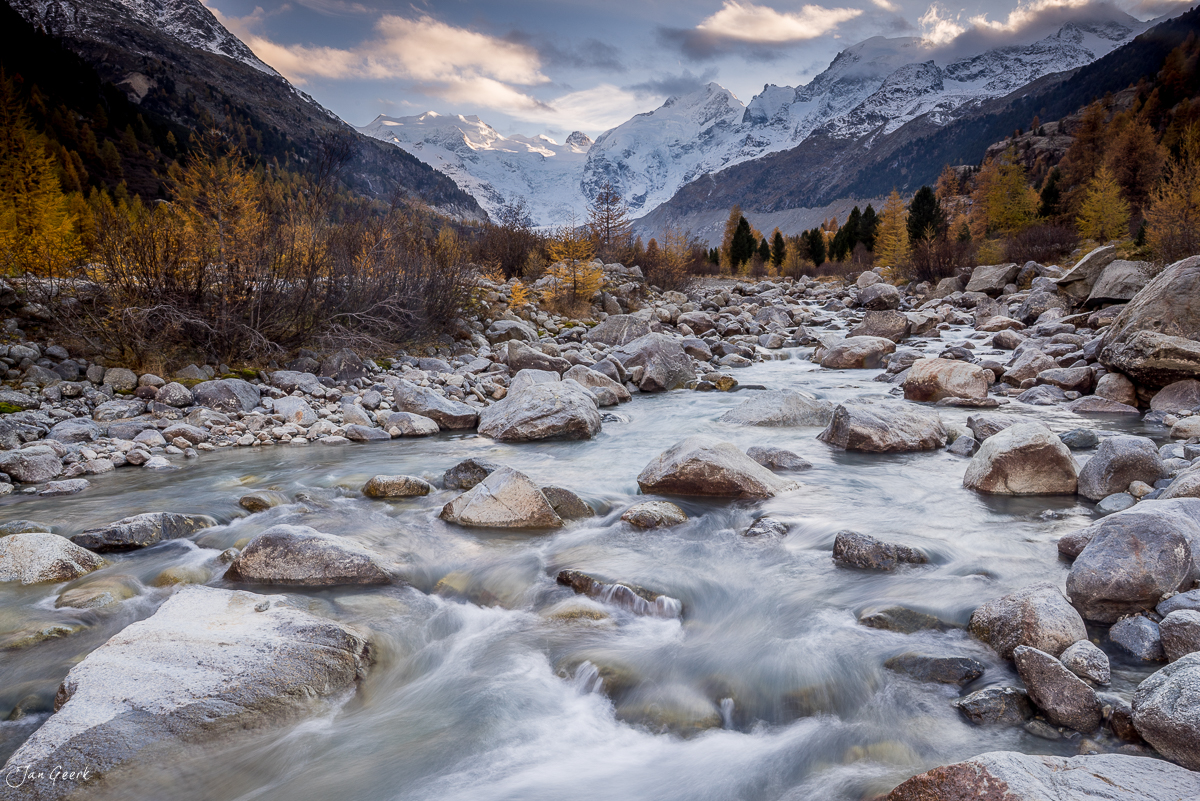 Wilde Bergbachlandschaft in Morteratsch mit schneebedeckten Gipfeln, goldenem Herbstlärchwald und Feldsteinen in der Herbststimmung, Graubünden Schweiz – Jan Geerk Fotograf Basel