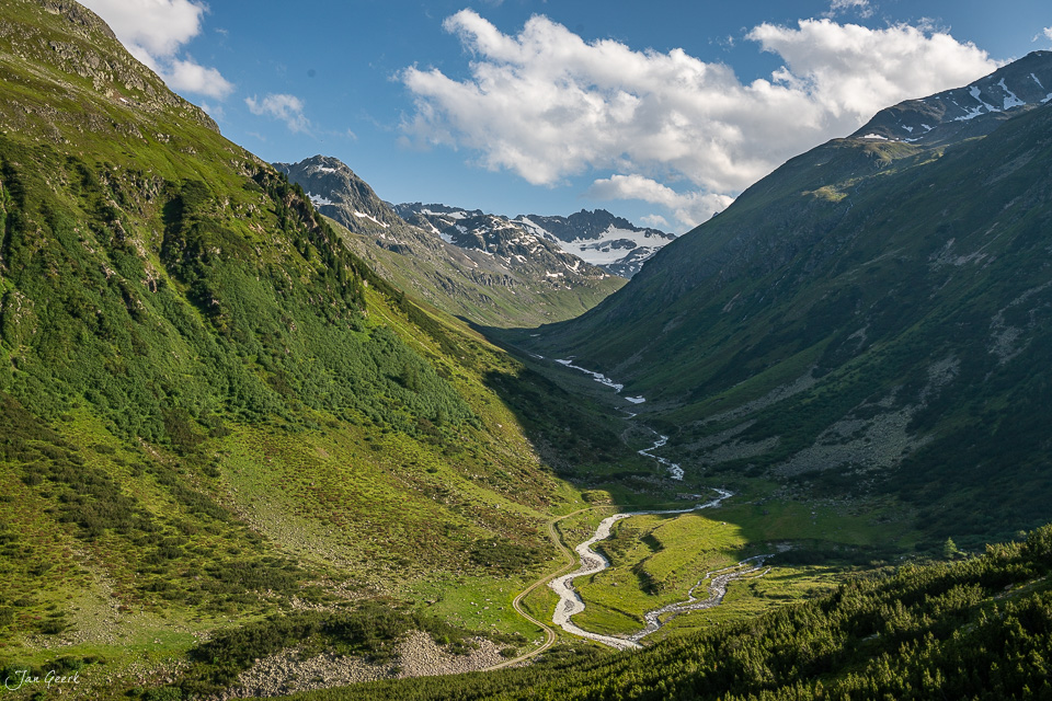 Serpentinen-Gebirgspass Flüelapass mit grünen Alpwiesen, schneebedeckten Gipfeln und Bergfluss im Sommer in Graubünden Schweiz – Jan Geerk Fotograf Basel