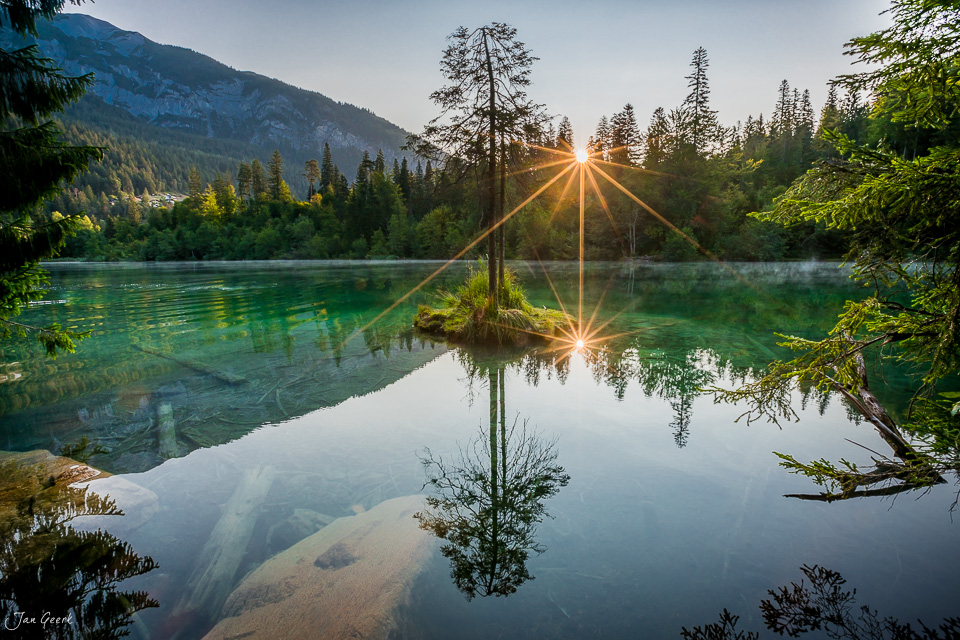 Spiegelnder Bergsee mit Lärchen bei Sonnenaufgang im Cresta See Flims Sommer Graubünden Schweiz – Jan Geerk Fotograf Basel