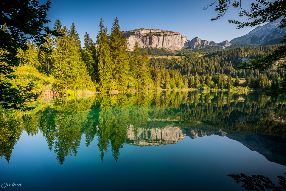 Spiegelglatter Bergsee mit Bergketten und Nadelwäldern im Sommer, Cresta See Flims Graubünden Schweiz – Jan Geerk Fotograf Basel