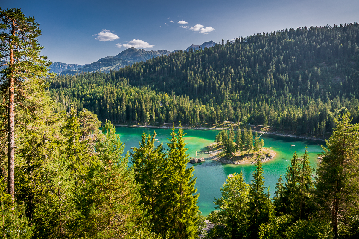 Bergsee mit türkisblauem Wasser umgeben von dichten Nadelwäldern und Bergen, Sommerlicht in Flims Graubünden Schweiz – Jan Geerk Fotograf Basel