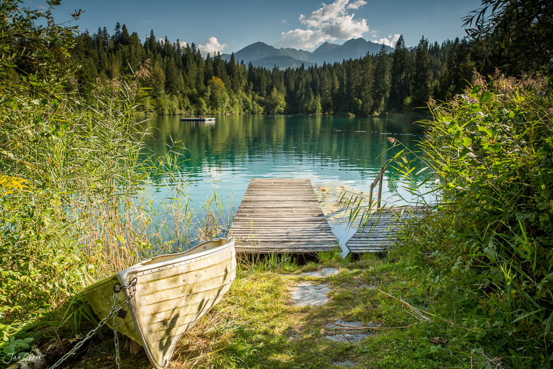 Holzboot am Ufer des Crestasee mit Holzsteg, Berwald und Bergen im Hintergrund, Sommerlichtstimmung, Graubünden Schweiz – Jan Geerk Fotograf Basel