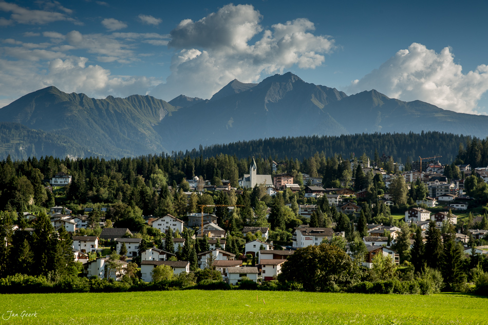 Bergdorf Flims mit Häusern und Kirche unter grünen Wiesen, Berge im Hintergrund, Graubünden Schweiz – Jan Geerk Fotograf Basel
