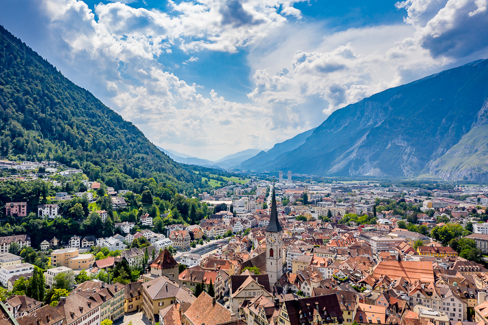 Luftaufnahme der Altstadt Chur mit Kirchturm, umgeben von grünen Bergen im Rheintal, Sommerlicht, Graubünden Schweiz – Jan Geerk Fotograf Basel