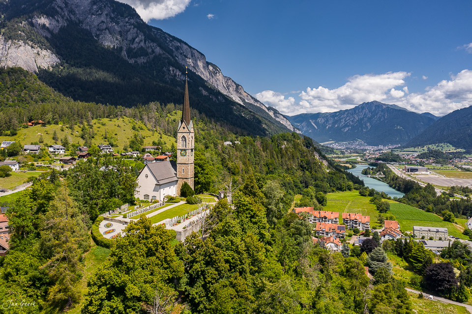 Kirche mit Spitzturm in Tamins im Churer Rheintal umgeben von grünen Bergen und Wäldern, Sommerluft bei Sonnenschein – Jan Geerk Fotograf Basel