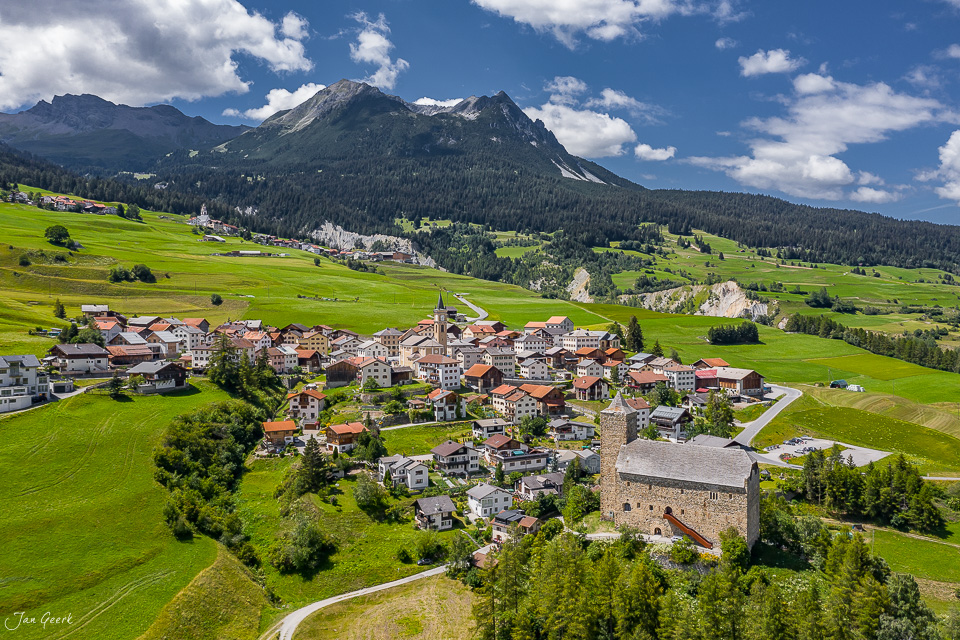 Luftaufnahme Dorf Cunter mit Burgturm, grüne Sommerwiesen, Berge im Hintergrund Graubünden Schweiz Jan Geerk Fotograf Basel