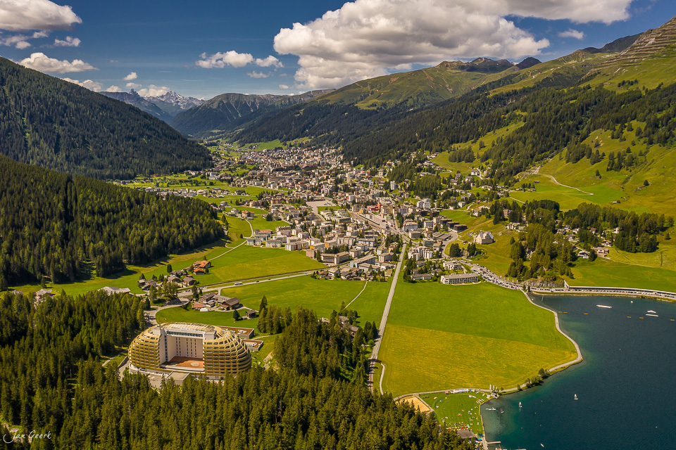 Luftaufnahme der Ortschaft Davos mit Davosersee, grüne Berghänge, Nadelwälder und schneebedeckte Gipfel im Sommer, Graubünden Schweiz – Jan Geerk Fotograf Basel