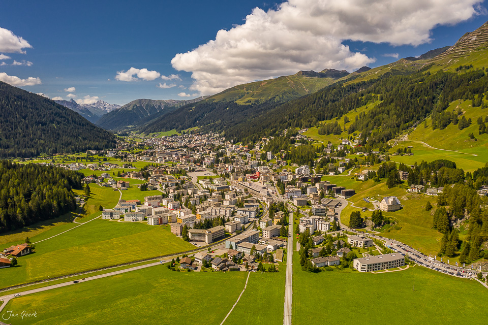 Luftaufnahme der Stadt Davos mit grünen Alpenwiesen, Bergwald und Sommerlicht in Graubünden Schweiz – Jan Geerk Fotograf Basel