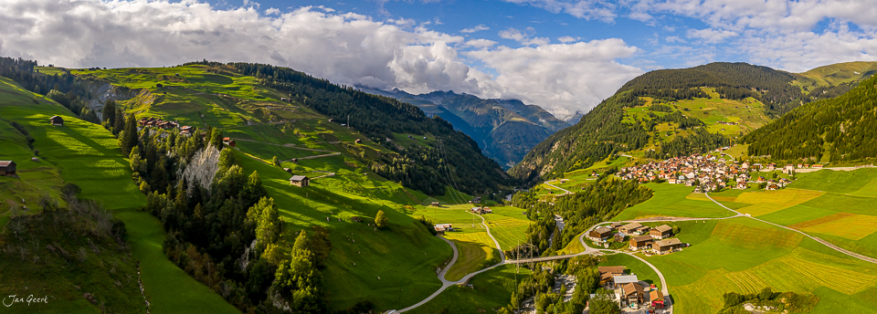 Luftaufnahme des grünen Alpentals Disentis mit Bergdörfern, Wäldern und Berggipfeln bei Sonnenschein – Graubünden Schweiz – Jan Geerk Fotograf Basel