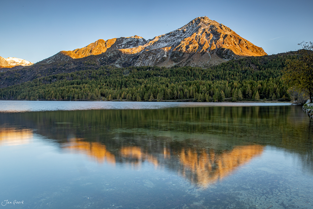Bergsee mit Spiegelung und schneebedecktem Gipfel im goldenen Morgenlicht, Engadin Graubünden Schweiz – Jan Geerk Fotograf Basel