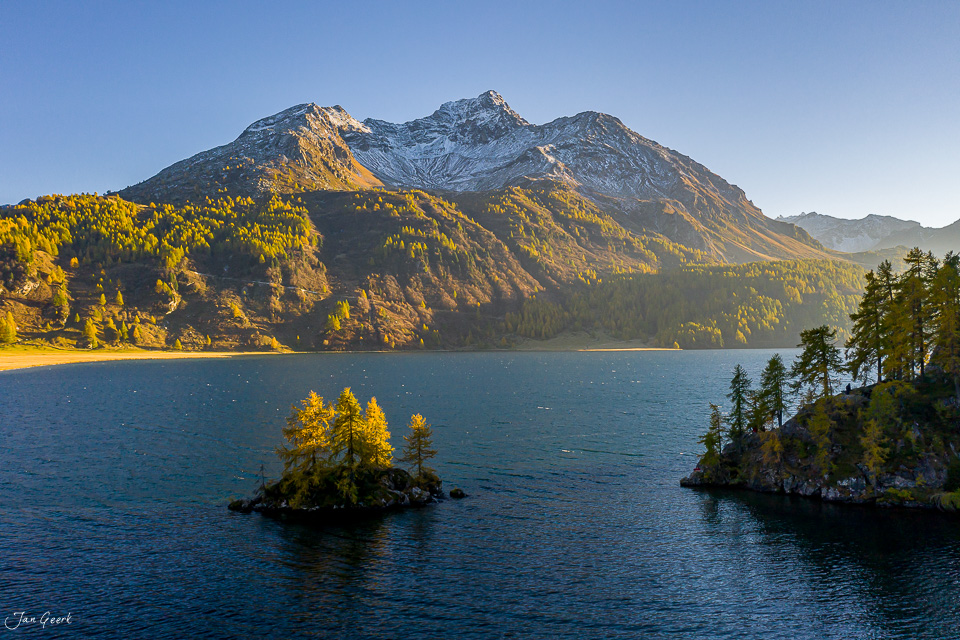 Herbstliche Bergsee-Landschaft mit schneebedecktem Gipfel, Lärchenwäldern und kleiner Insel im Silsersee, Engadin Graubünden Schweiz – Jan Geerk Fotograf Basel