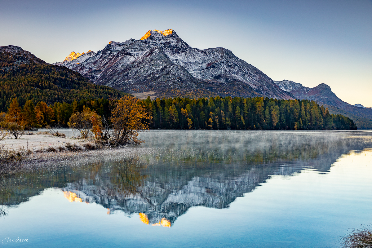 Berglandschaft am Silsersee mit schneebedecktem Gipfel, Herbstwald und Spiegelung im Wasser, Engadin Graubünden Schweiz – Jan Geerk Fotograf Basel