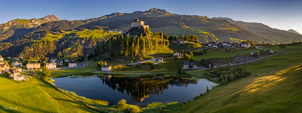 Schloss Tarasp über einem See in goldener Sommersonne, umgeben von grünen Alpenwiesen und Bergen im Engadin Graubünden Schweiz – Jan Geerk Fotograf Basel