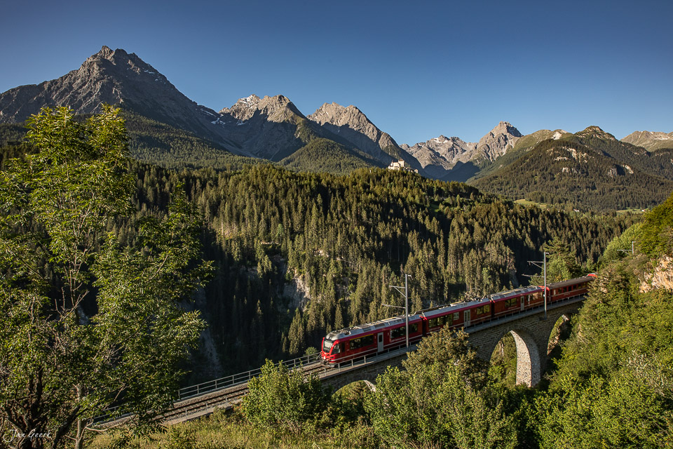 Güterzug überquert auf Steinbogenbrücke Tal in Tarasp mit Alpengipfeln und Nadelwäldern, Sommerlichtstimmung, Graubünden, Schweiz – Jan Geerk Fotograf Basel