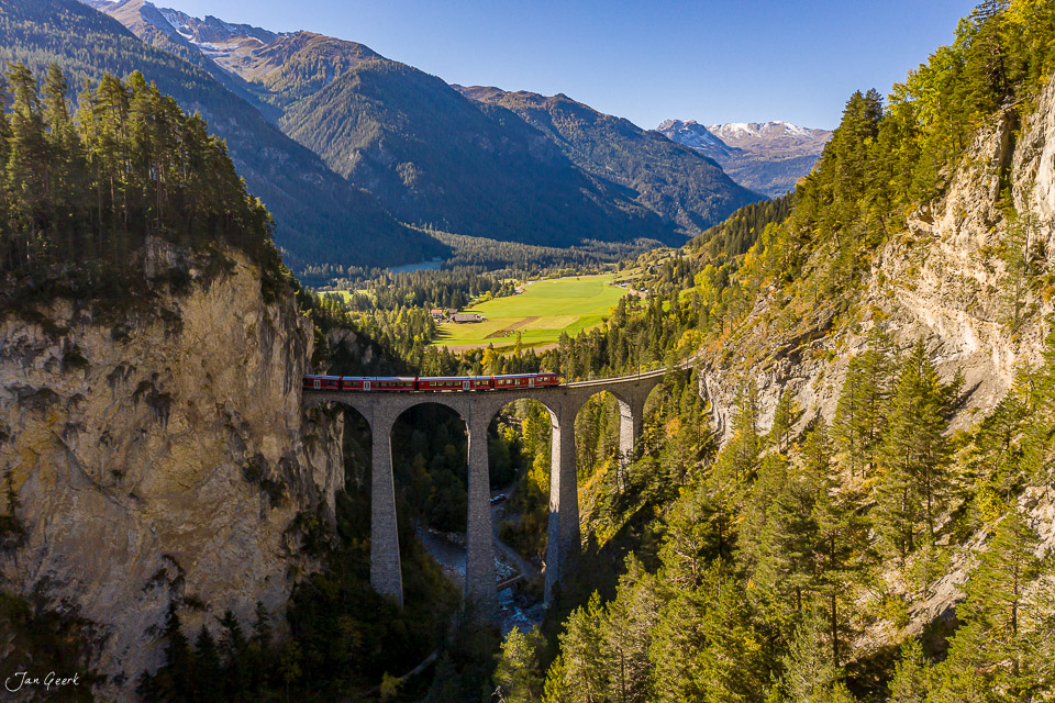 Roter Zug auf Landwasserviadukt über Bergtal mit grünen Wäldern, sonnige Herbststimmung Graubünden Schweiz – Jan Geerk Fotograf Basel