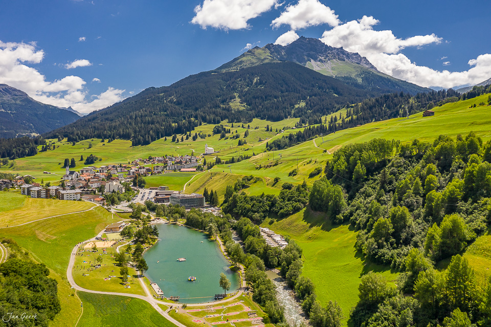 Luftaufnahme Savognin mit türkisem See, Bergdorf und Piz Platta im Sommer, Graubünden Schweiz – Jan Geerk Fotograf Basel
